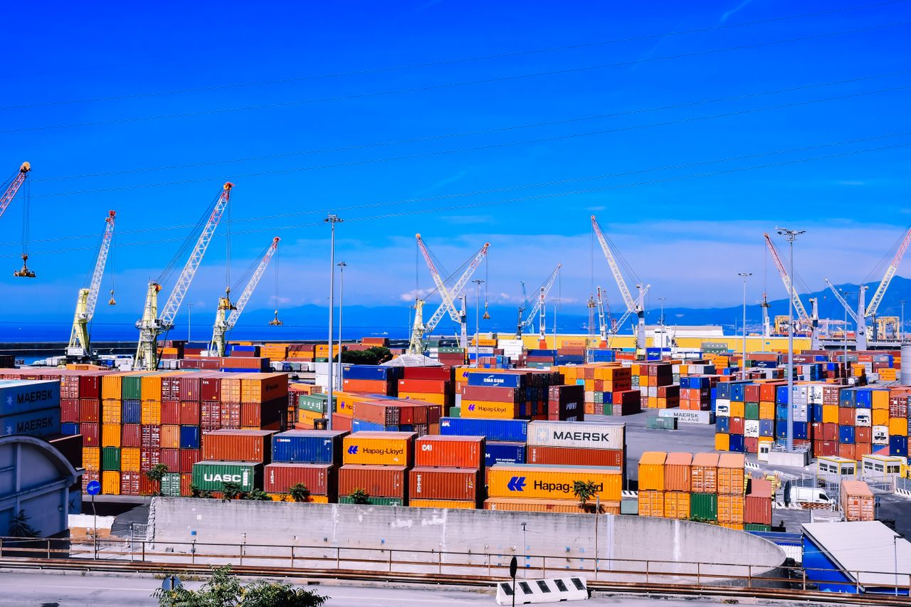 Home A bustling shipping port with colorful stacked containers and numerous cranes under a clear blue sky.