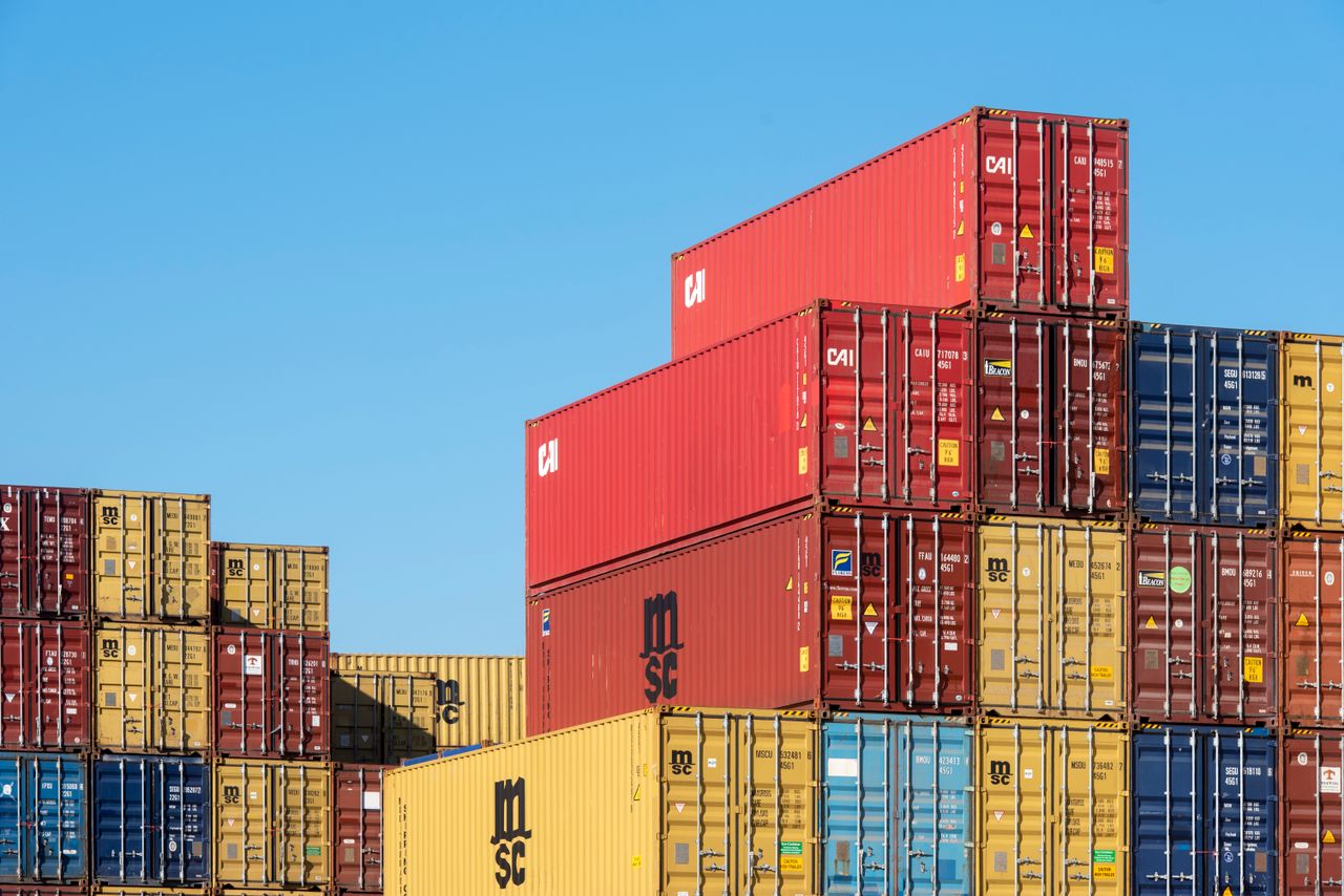 Home A vibrant collection of stacked shipping containers under a clear, blue sky. Ideal for logistic themes.