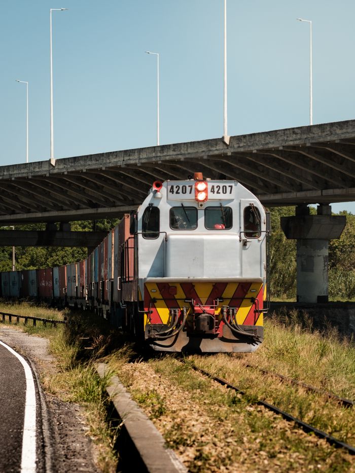 Freight train passing under a bridge in Laguna, Brazil, during daylight.