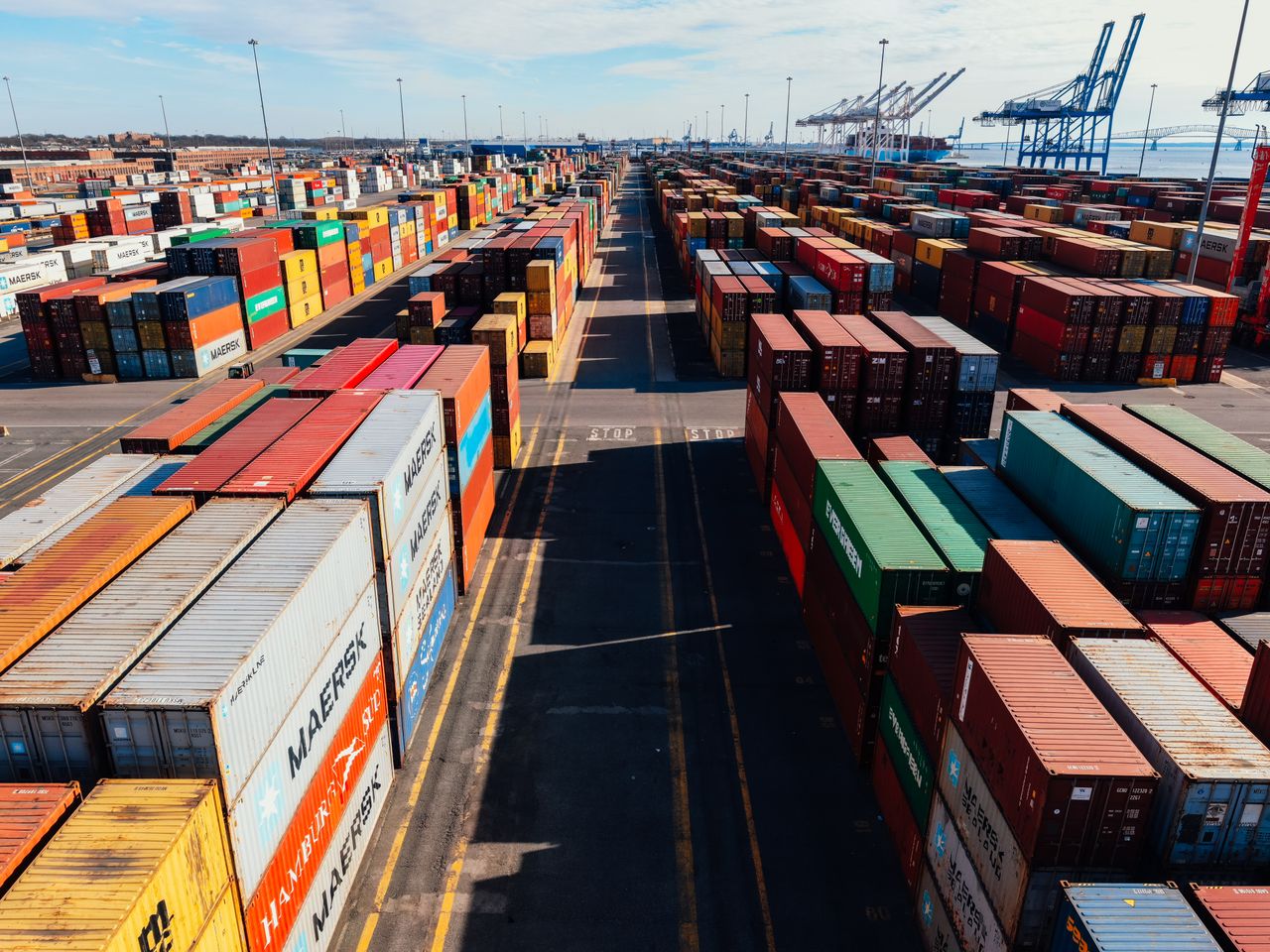 From above of asphalt roadway among large colorful metal containers placed in industrial area under cloudy sky in sunny day